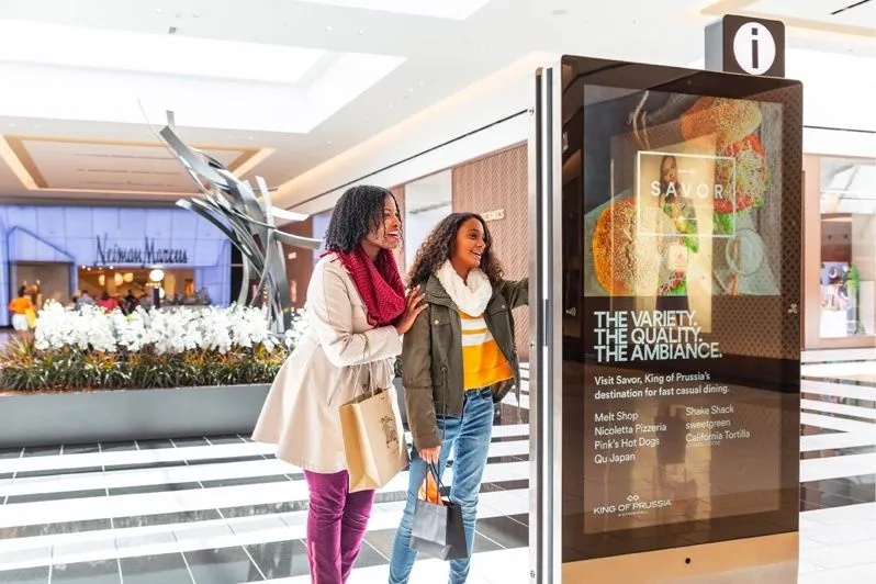 Clientes pasando junto a una pantalla publicitaria digital en un centro comercial