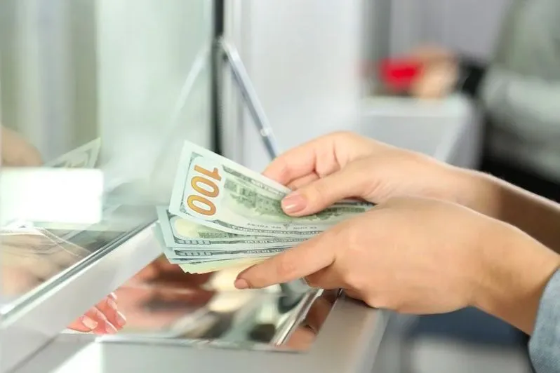 Cliente contando billetes de dólar en el mostrador de un banco
