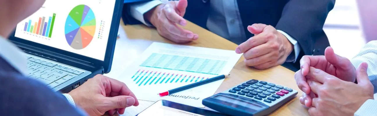 Personas revisando gráficos financieros en un escritorio con una calculadora