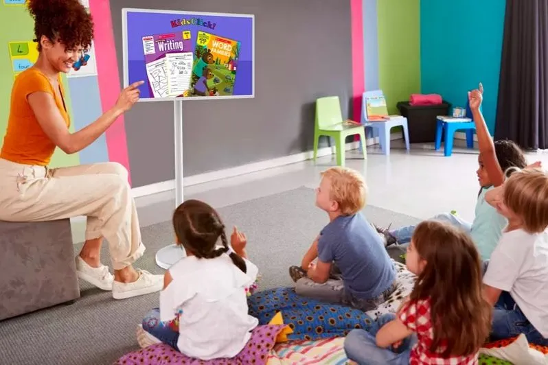 Profesora y niños en un aula con una pantalla sobre un soporte