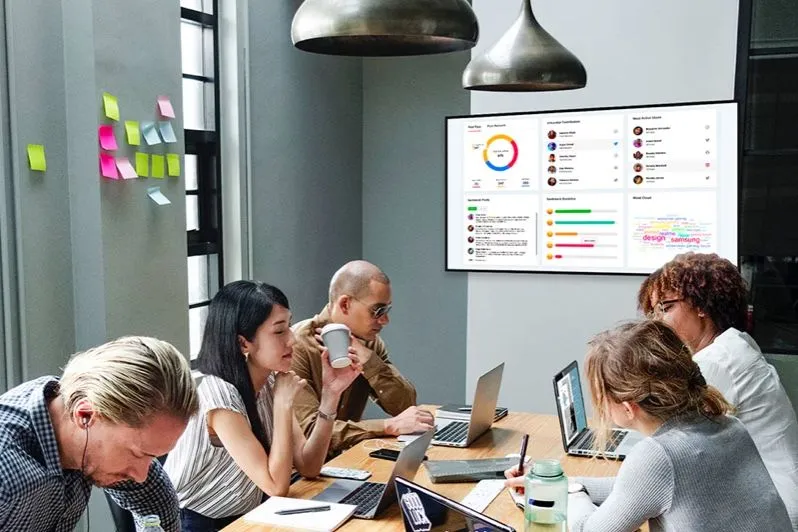 Reunión de equipo bajo una pantalla con paneles de datos de la empresa