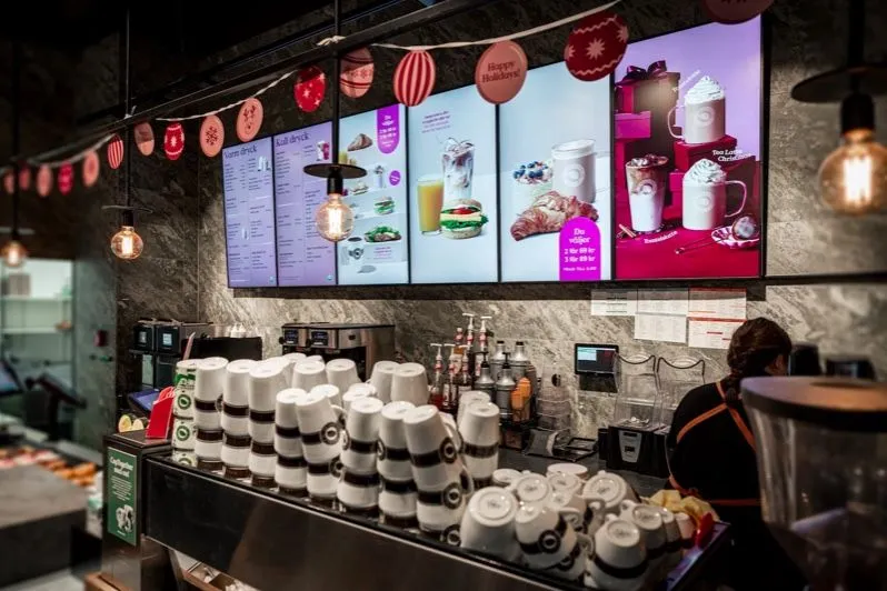 Barra de una cafetería con una hilera de pantallas con el menú digital